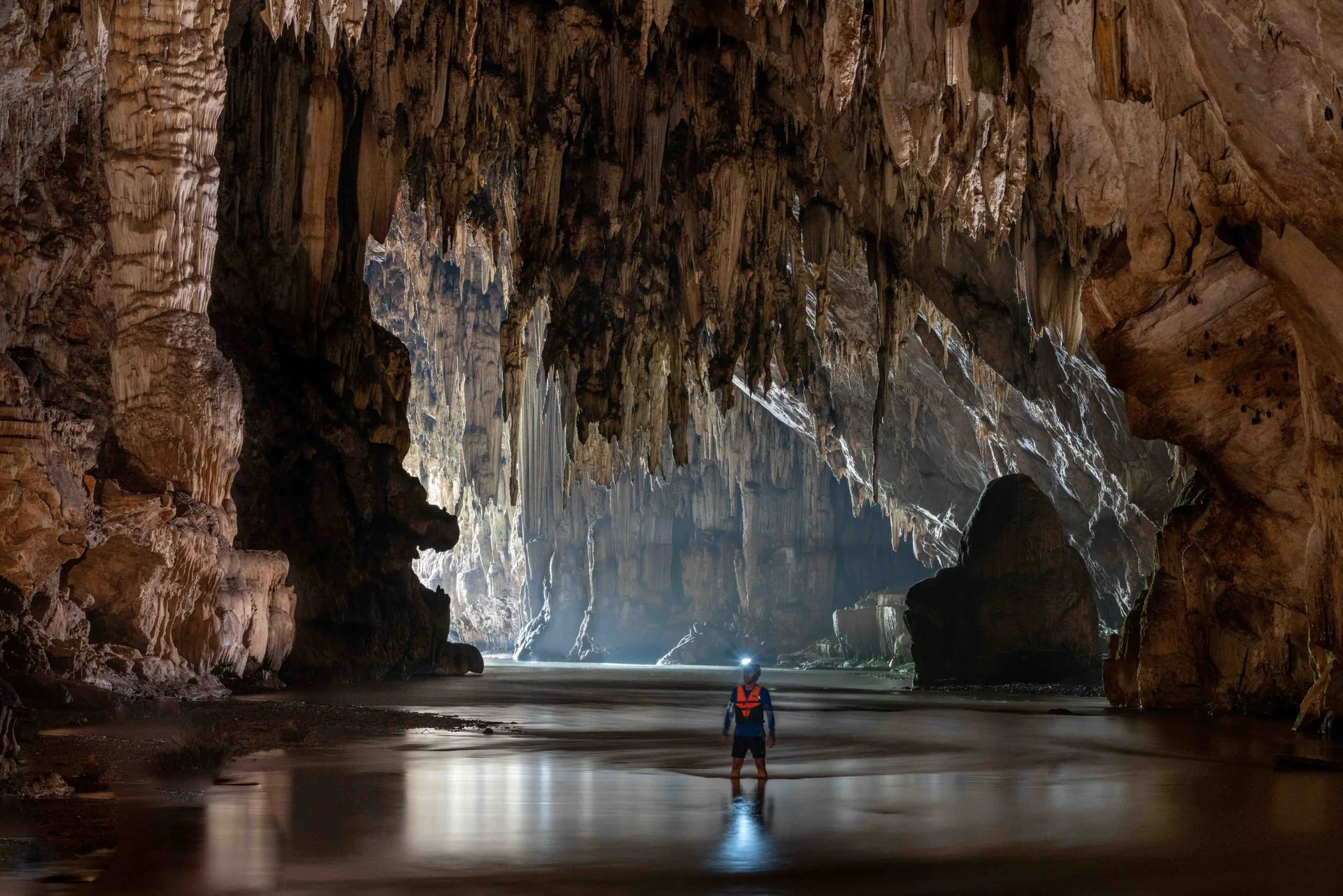 Explorer standing in the still water of a vast limestone cave in Pang Mapha