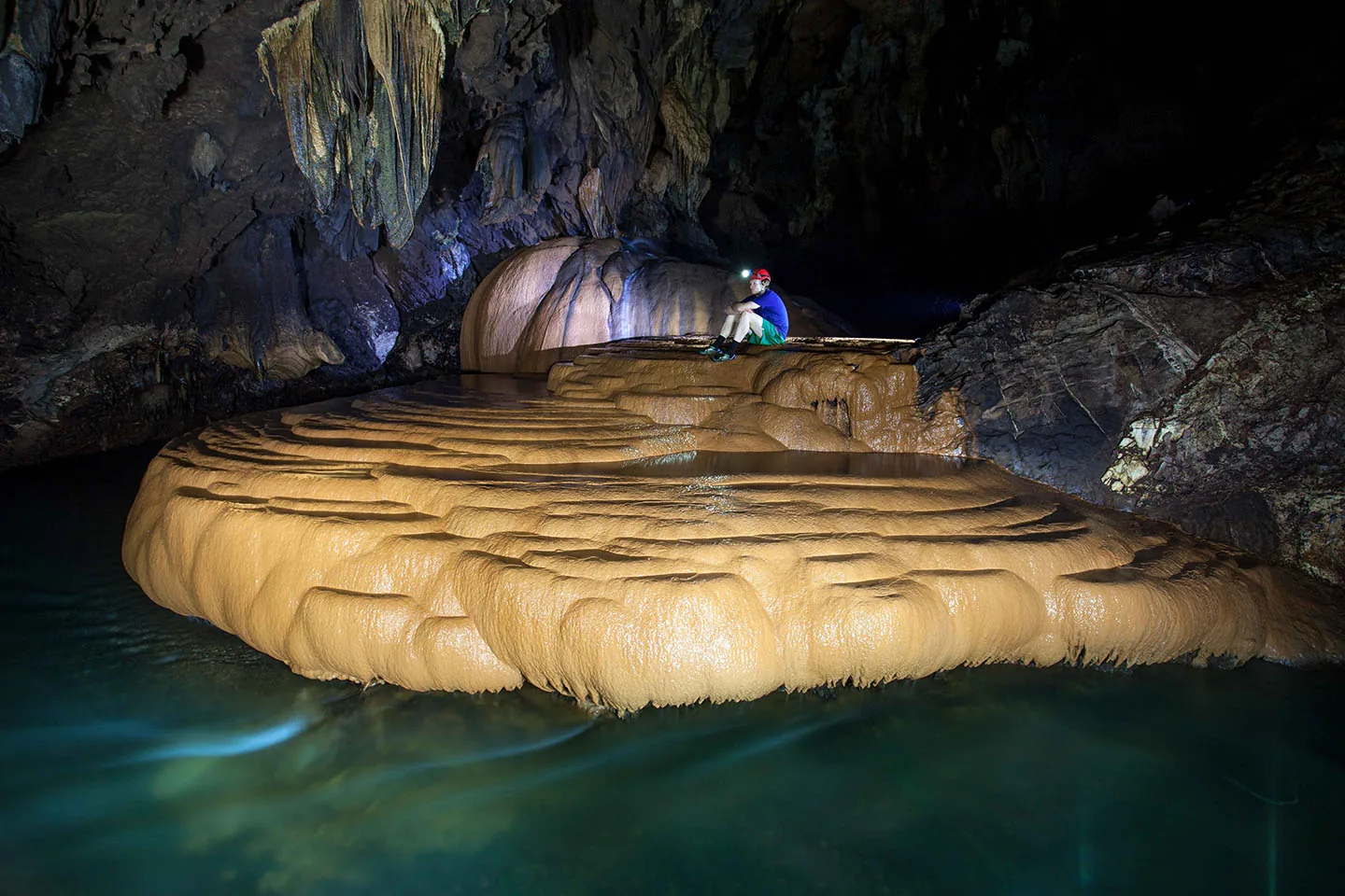 Caver above a golden rimstone formation and turquoise pool