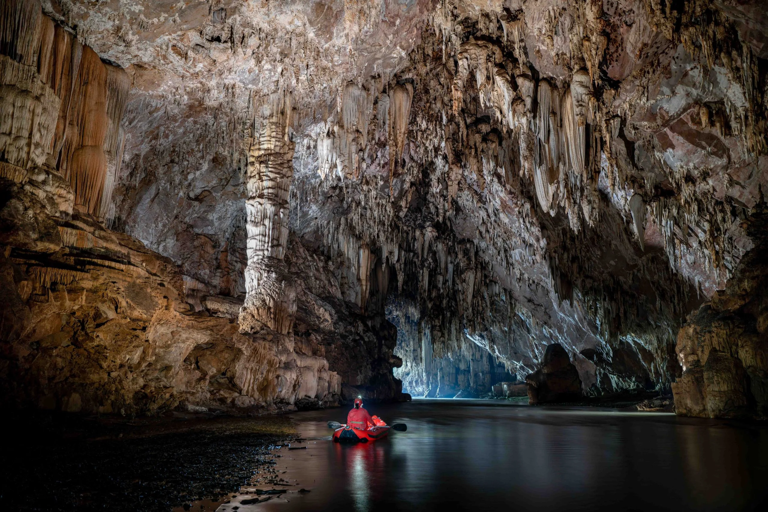 Kayaker on an underground river in a huge limestone cave chamber